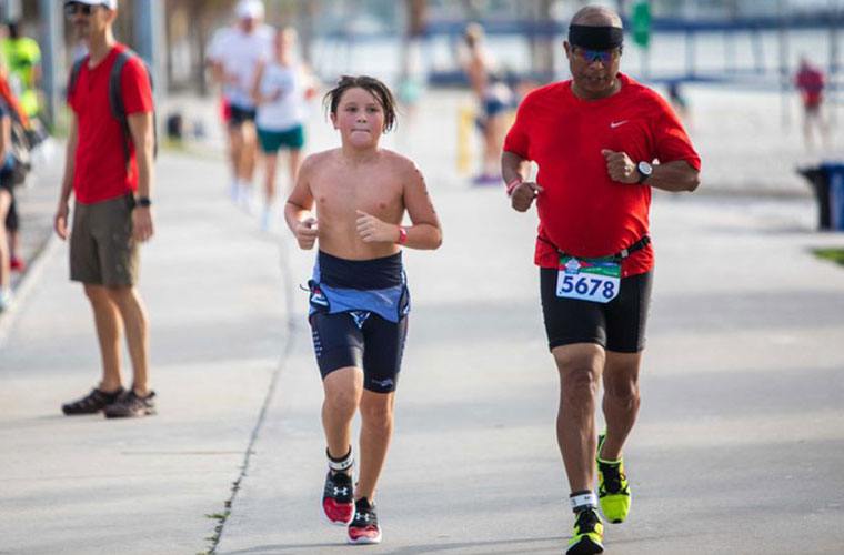 A young boy and an older man dressed in athletic clothing run side by side in a race.