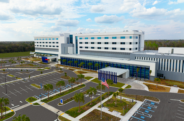 An aerial view of the new South Florida Baptist Hospital in an empty parking lot. The building is large and rectangular.