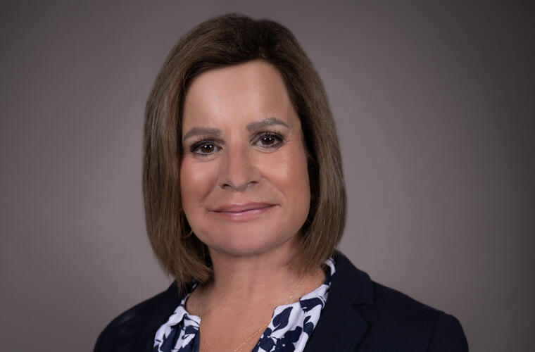 Headshot of a woman with short, brown hair wearing a navy-blue jacket over a white and blue blouse.