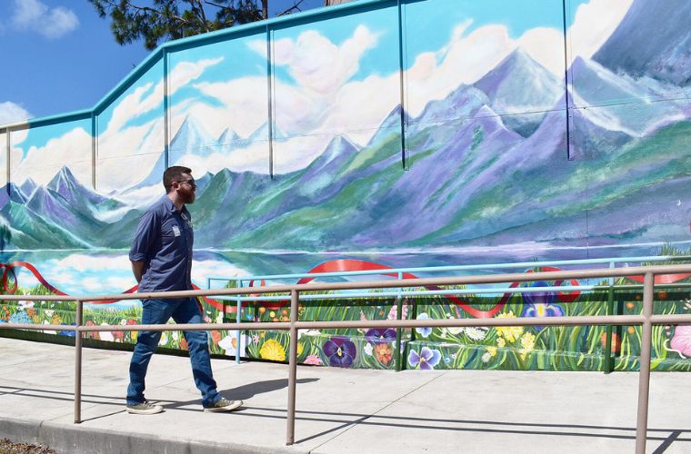 A man walks along and admires a mural of mountains and water on a hospital wall.