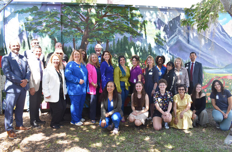 A large group of diverse individuals smiling and posing for a photo in front of a vibrant mural.