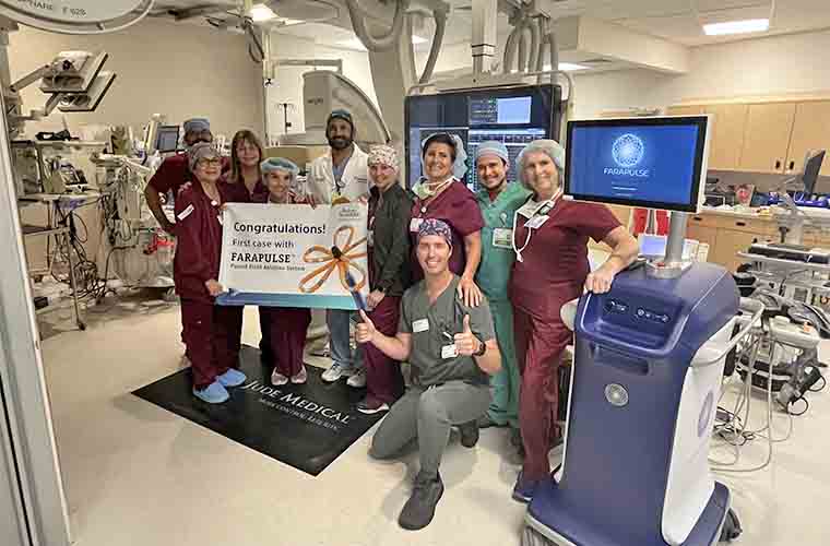Ten hospital team members in scrubs are standing in an operating room holding a sign that says, "Congratulations! First case with FARAPULSE."