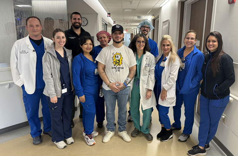 A group of men and women dressed in hospital scrubs and some in doctor’s coats surround a young man who is a patient.