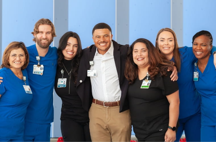 A diverse group of health care professionals in business attire and blue and black scrubs.