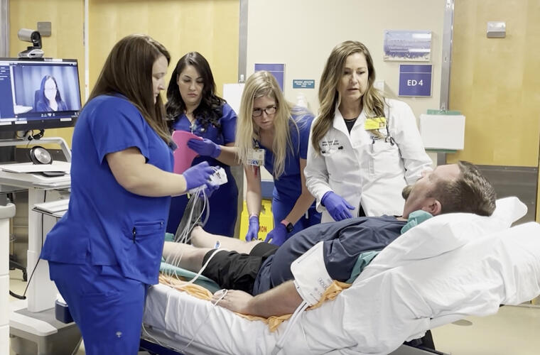 A man is in the hospital, on a stretcher, while a physician and several nurses attend to him.