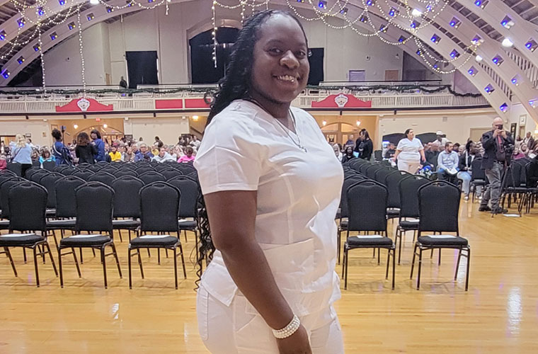A Black woman dressed in white stands inside a room with many lights hanging from the ceiling.