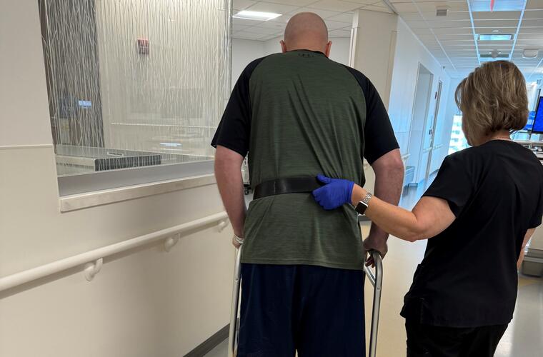 A man walking with a walker is assisted by a nurse. 