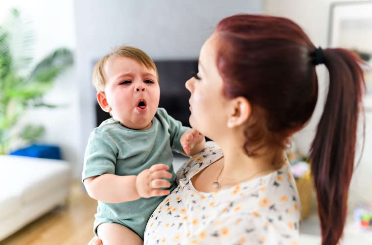 A mother is holding a sick baby in the living room while the baby is coughing.