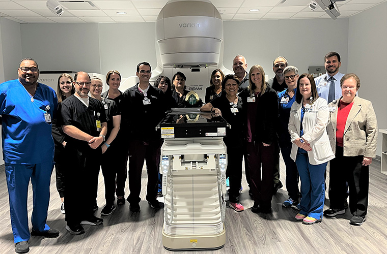 A group of people – some dressed in hospital scrubs – stand around a new piece of equipment in a room. 