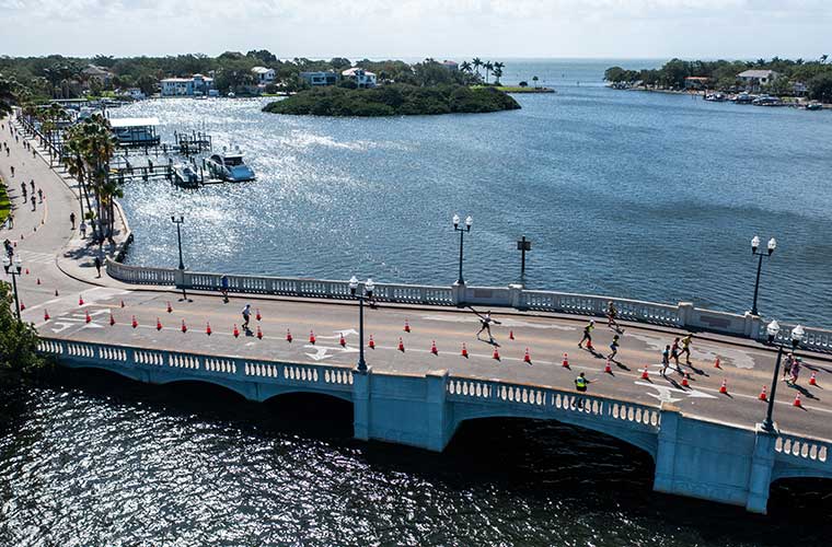 Athletes run on a bridge set against beautiful blue water.