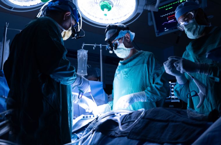 Two surgeons in blue scrubs and masks performing surgery on a patient in an operating room.
