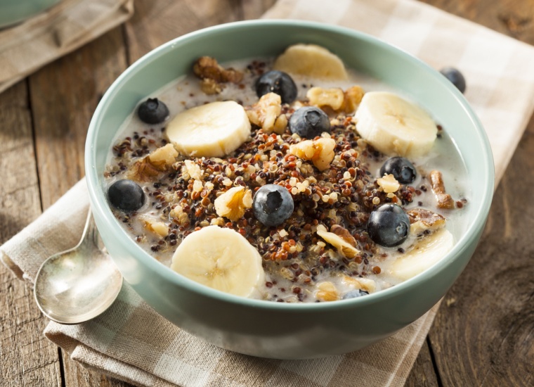 A bowl filled with quinoa, blueberries and banana slices sits on a rustic wooden table.