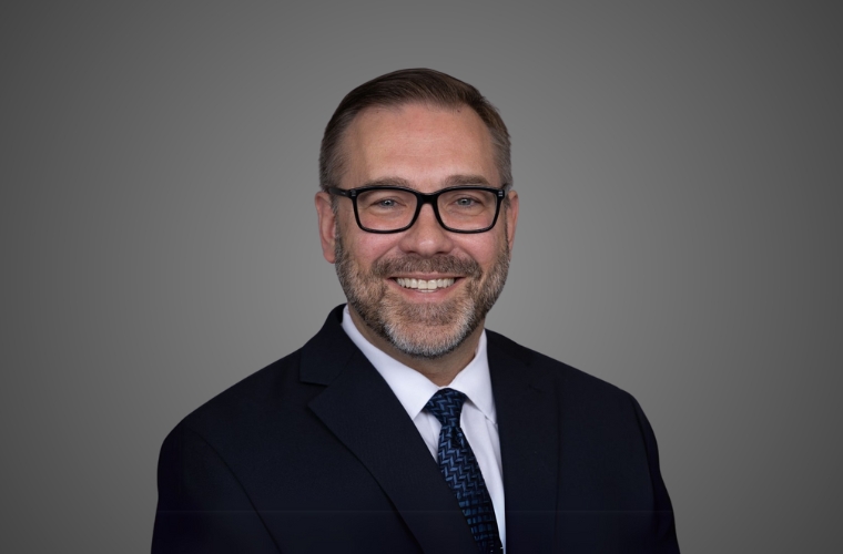 A professional smiling headshot of Dr. Robert Kopec smiling. He is wearing glasses with a dark colored suit, white shirt and dark blue tie.   