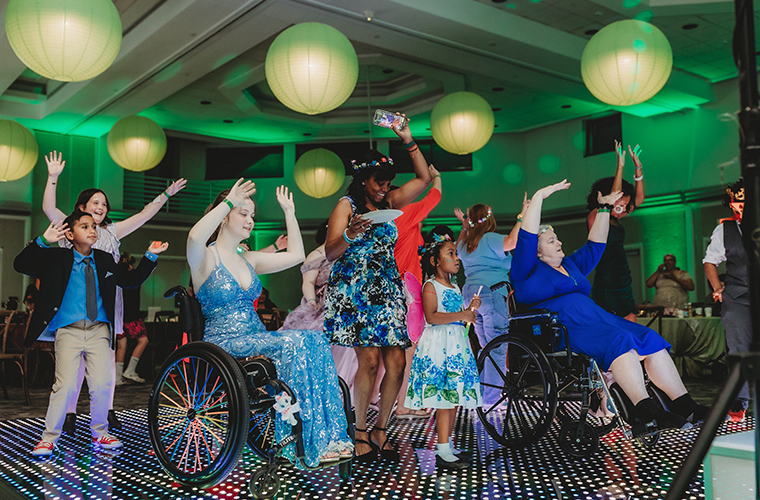 A diverse group of children and adults, some in wheelchairs, dancing on a vibrant dance floor.