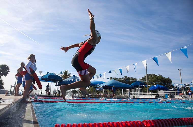 A young athlete dressed in a swimsuit jumps into the pool during a competition.