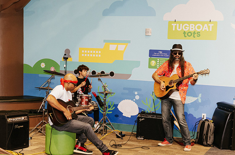 Two men and a teenage boy joyfully playing various musical instruments in a warm, inviting room setting.