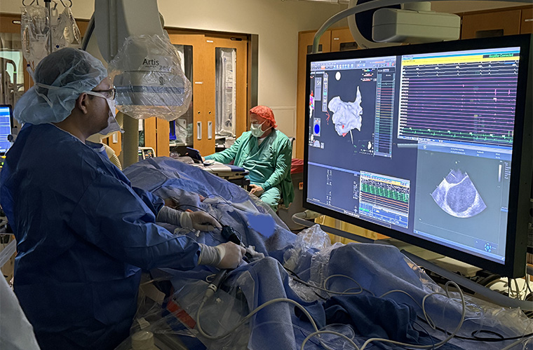A surgeon looks at a monitor while performing surgery. Another team member in scrubs and a red surgical cap is in the background. 