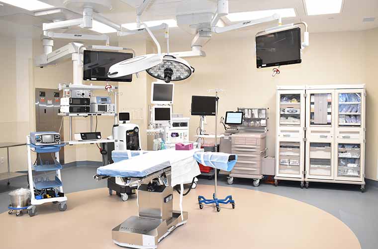 Interior of a modern hospital surgical room equipped with state-of-the-art medical devices, operating table, overhead surgical lights, and monitoring screens.