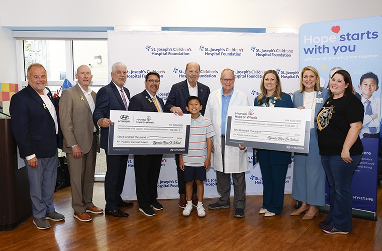 A group of men and women and a boy hold up large checks during an award ceremony.