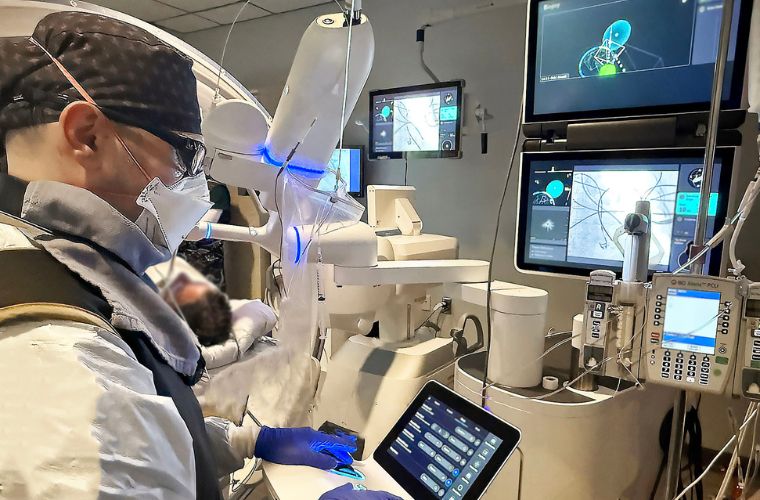 A health care professional operates a surgical robot in a modern medical room equipped with advanced monitors displaying real-time data and imaging.