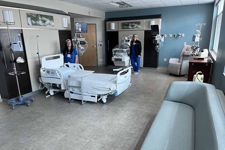 Two health care professionals are standing in a modern hospital room equipped with medical beds and advanced monitoring equipment.