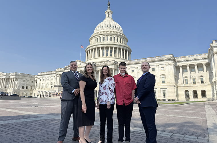 Two men, two women and a teen boy stand in front of the U.S. Capitol building. 
