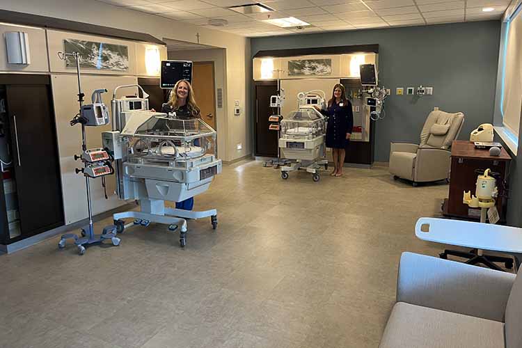 Two individuals standing in a modern hospital nursery with two infant incubators and medical equipment.