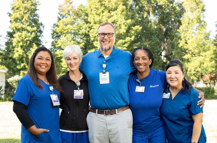 A group of five BayCare team members are hugging and smiling together.