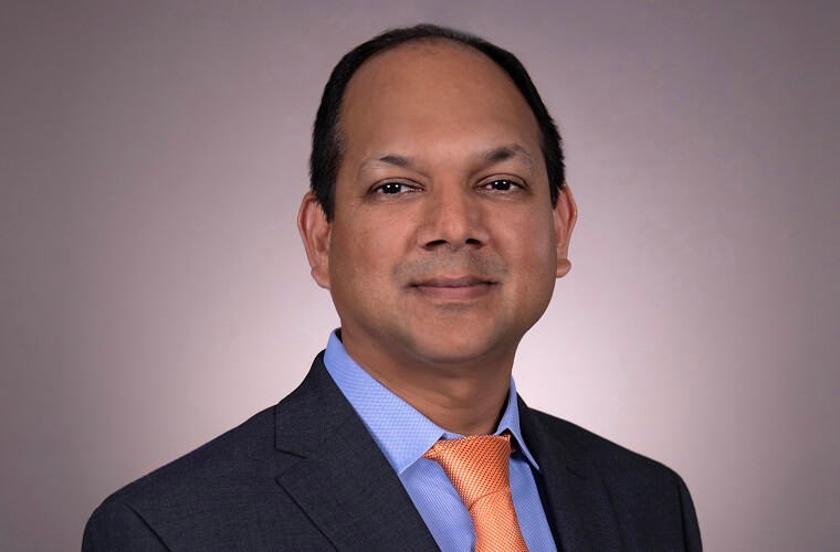 A man is wearing a dark suit, blue shirt and salmon-colored tie.