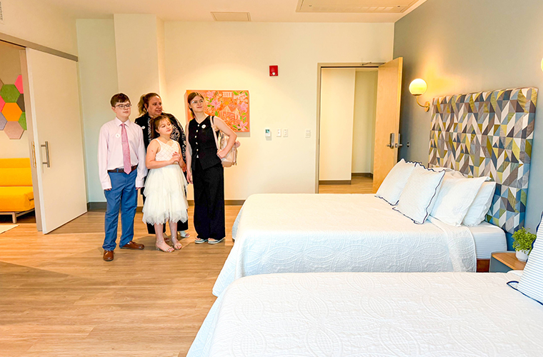 A young boy and two young girls with an older lady stand together in a bedroom.