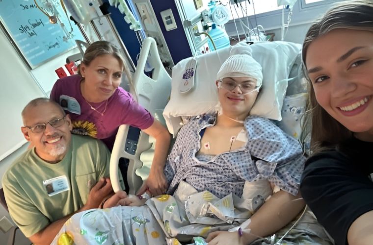 A family of four with the patient in the center gather for a photo in a hospital room.