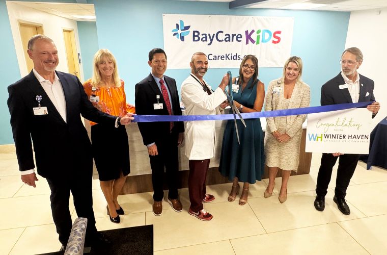 A group of eight people stand together at a ribbon-cutting ceremony for a new hospital wing.