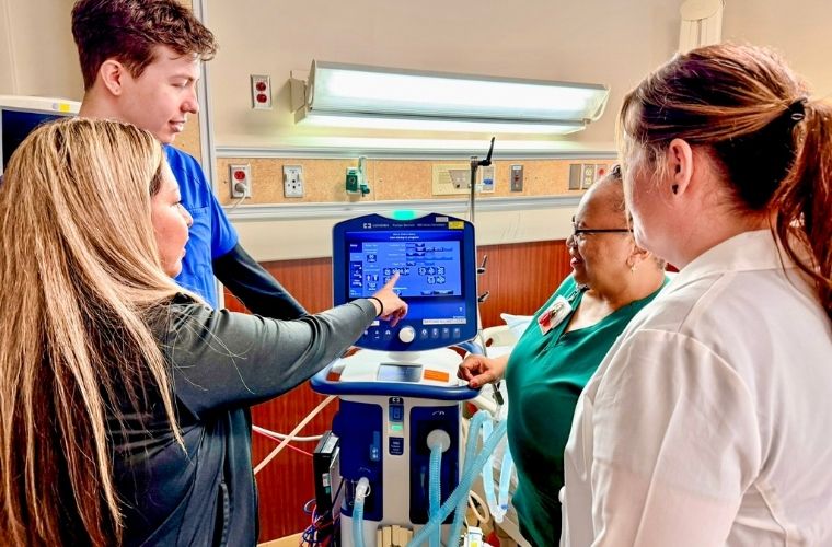 Clinical team members reviewing settings on a hospital respiratory care machine.