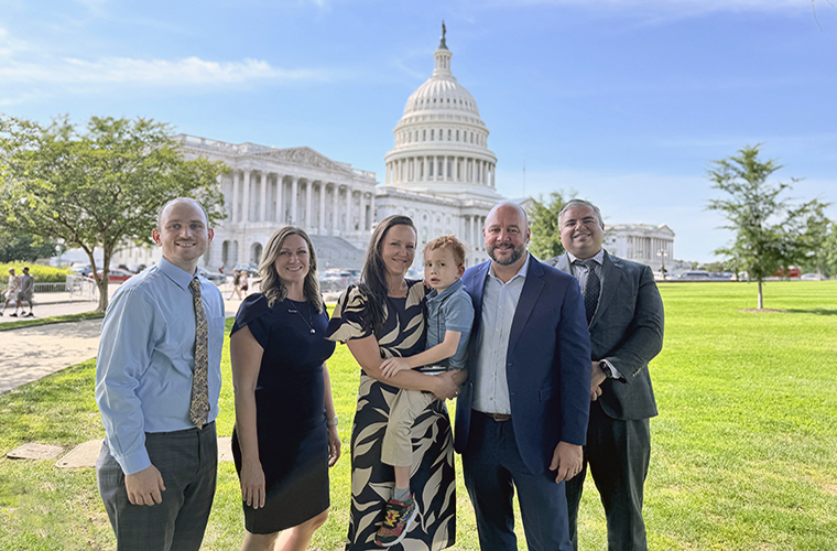 Three men and two women are standing in front of the U.S. Capitol building. One woman is holding a young boy in her arms.