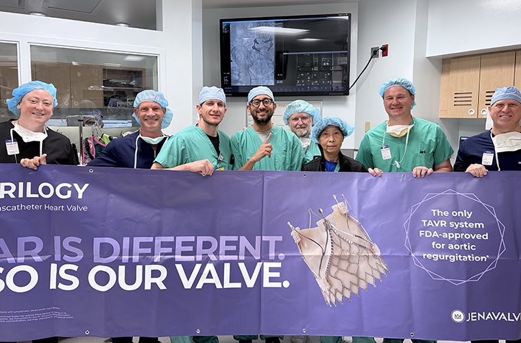 Eight people in scrubs and surgical caps stand behind a purple banner with information on heart valves.