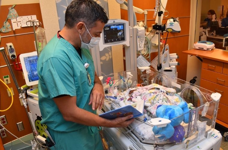 A doctor reads from a children’s book beside a newborn in a neonatal intensive care unit.