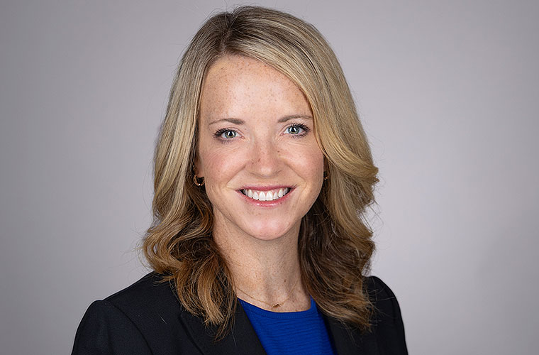 Smiling woman with blond, wavy hair wearing a black suit jacket.