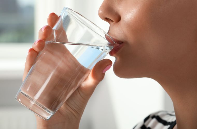 Closeup of woman drinking a glass of water indoors.