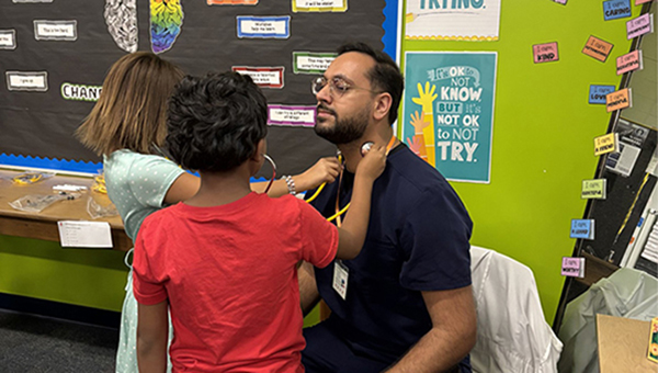 Elementary students practice listening through stethoscopes. Their patient is a BayCare resident physician who was participating in the Great American Teach In.