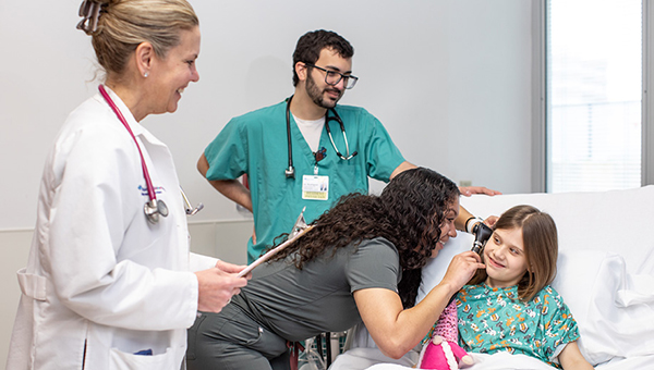 A faculty member watches as a resident looks inside the ear of a pediatric patient.