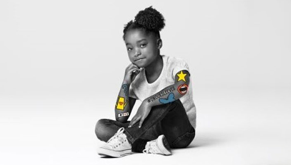A young girl sitting on the floor with her arms crossed, participating in the "On Our Sleeves" campaign for mental health awareness.