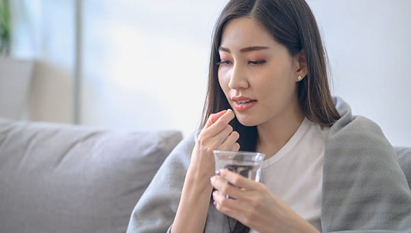 A young woman has the flu and is taking medicine with a glass of water.