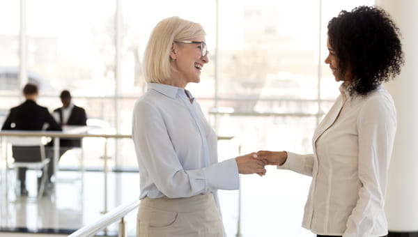 On her first day at work, a young woman is shaking hands with her female supervisor.