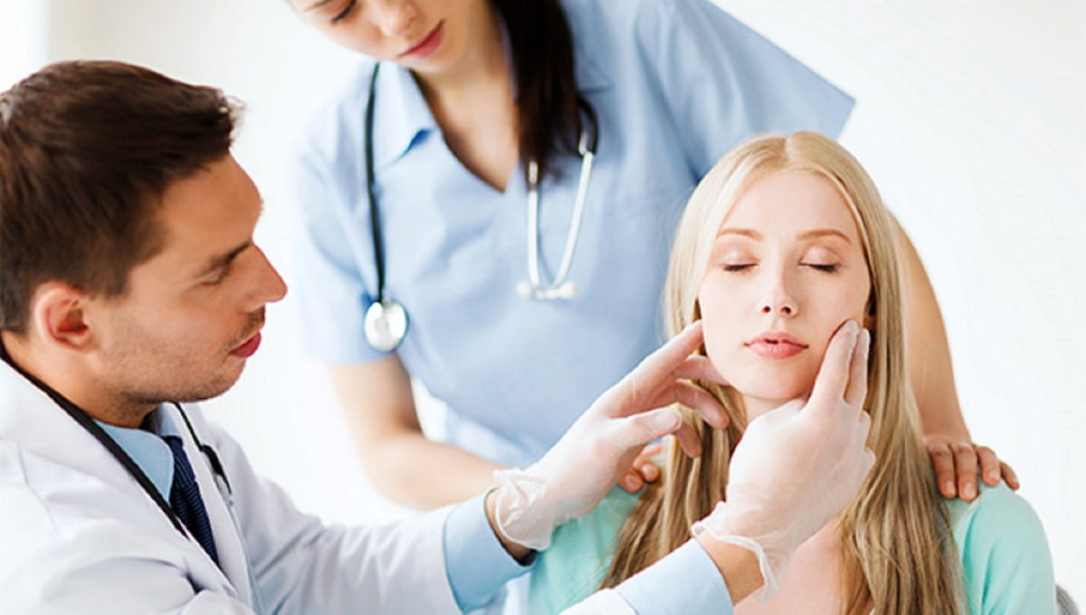 A cosmetic surgeon points to the face of a female patient.