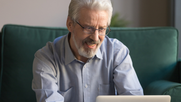 Close up grey haired smiling mature man wearing glasses looking at laptop screen