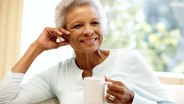 older woman smiling and sitting while holding mug