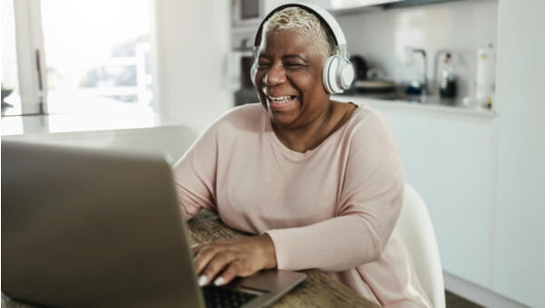 a woman smiling and sitting with her laptop with headphones on