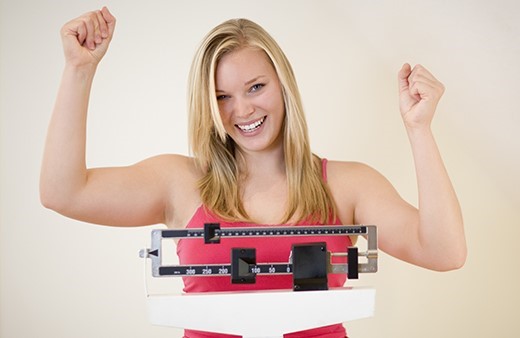 lady standing on a scale with her arms raised with success