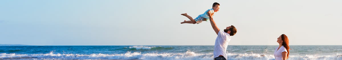 Man holding a child into the sky at the beach.