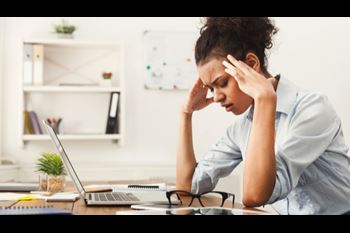 A young woman is visibly distressed while sitting at her desk in front of her laptop.